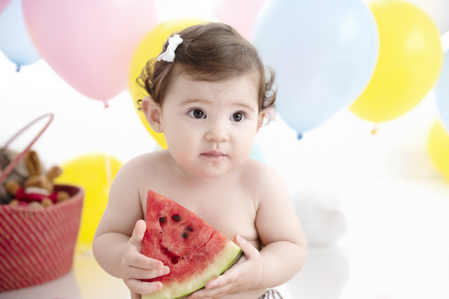 bebê com fatia de melancia menina fofa fundo com balão de frutas smash the fruit aniversário de 1 ano de criança fotos de família no estúdio de fotografia laura alzueta em São Paulo