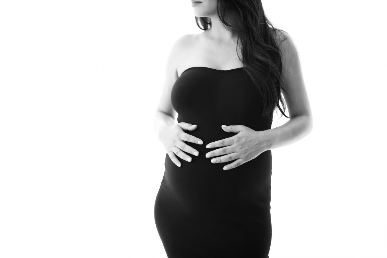 grávida com vestido preto e mãos na barriga em fotos de estúdio na zona oeste de sp pinheiros fotógrafa laura alzueta