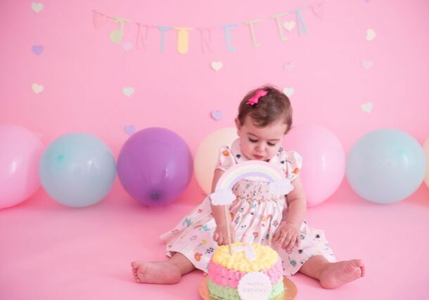bolo colorido com arco-íris bebê sentada em cadeira com fundo rosa com balões candy colors smash the cake laura alzueta estúdio de fotografia são paulo ensaio de fotos de aniversário de 1 ano de bebê menina